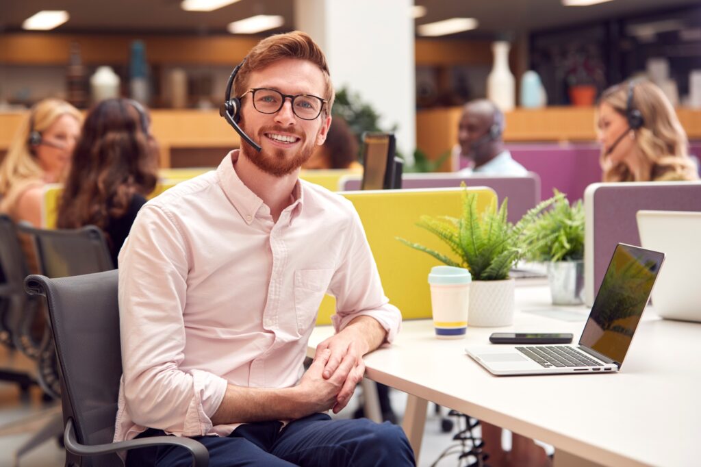 Portrait Of Businessman Wearing Headset Talking To Caller In Customer Services Centre